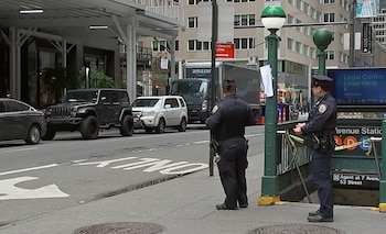 Dos agentes uniformados custodian la entrada a una estación de metro acordonada con cinta amarilla frente a una calle con tráfico