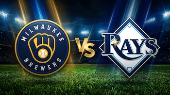 Logotipos de Milwaukee Brewers y Tampa Bay Rays separados por las letras Vs doradas sobre césped y un estadio nocturno iluminado.