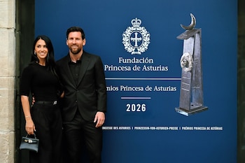 Lionel Messi y Antonela Roccuzzo posan de pie vestidos de negro frente a un panel azul con el emblema de la Fundación Princesa de Asturias