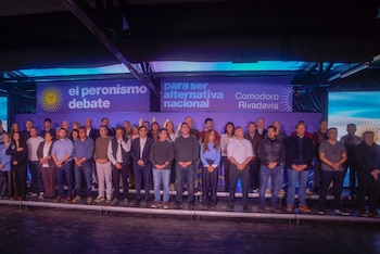 Un grupo de hombres y mujeres de pie en un escenario frente a un cartel del peronismo en Comodoro Rivadavia