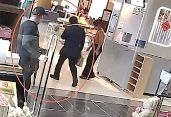 Tres personas caminan en el interior de un establecimiento; un hombre con gorra y sudadera, un hombre con traje oscuro y una persona con camisa naranja clara