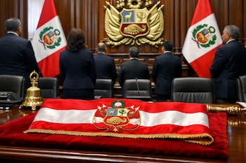 Una banda presidencial roja y blanca con escudo bordado sobre terciopelo rojo. Detrás, autoridades de espaldas, dos banderas peruanas y el escudo nacional.