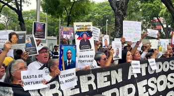 Una multitud de manifestantes, mayormente adultos, sostiene carteles con fotos de personas y textos como 'LIBERTAD' y 'BASTA DE TORTURAS' en una calle arbolada