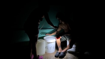 Una persona ilumina con una linterna roja a otra persona junto a dos bidones de plástico blanco en una habitación oscura