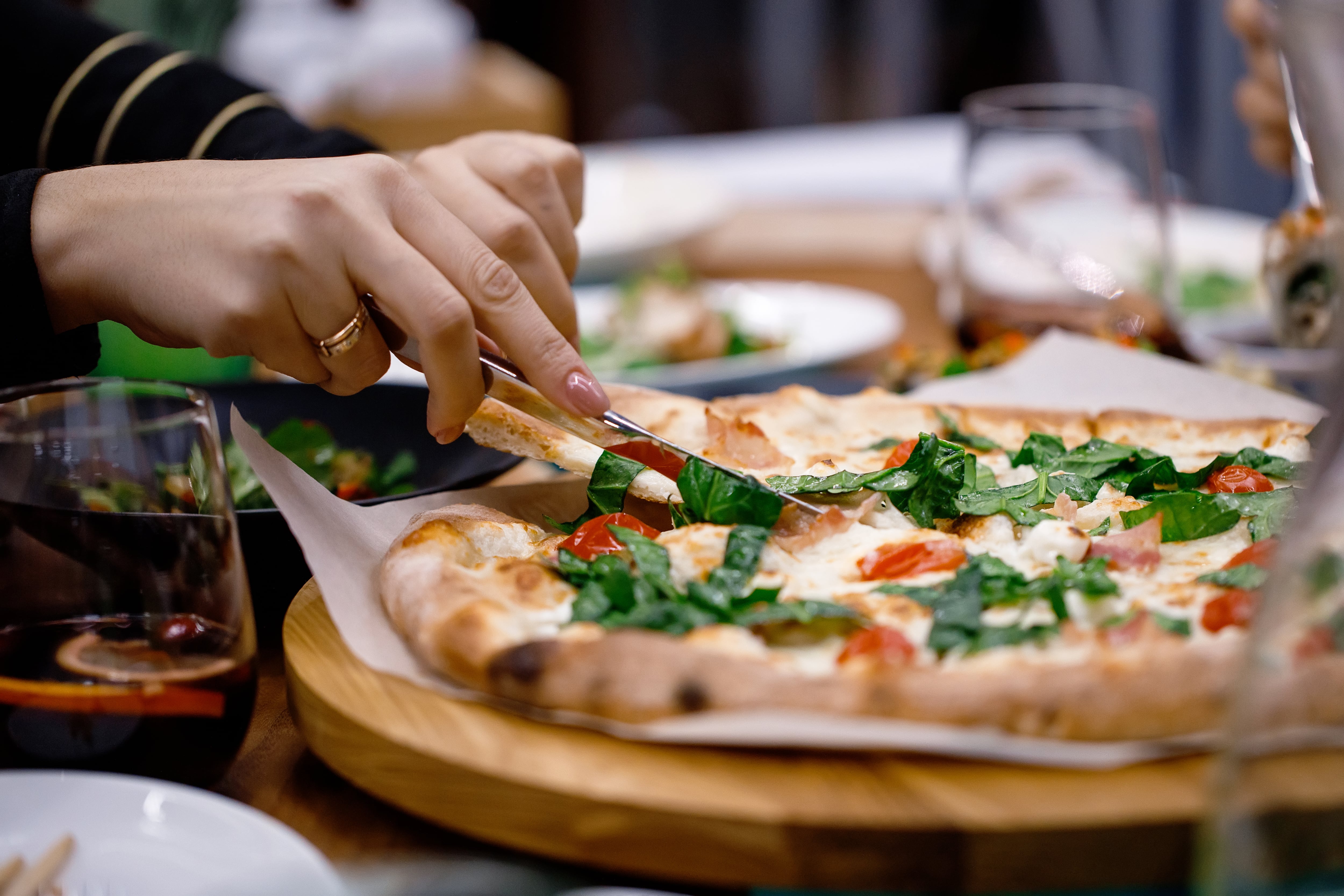 Una mujer corta un trozo de una pizza de verduras (AdobeStock)