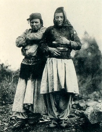 Fotografía en blanco y negro de dos personas vestidas con ropas tradicionales albanesas de pie al aire libre