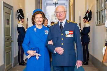 El Rey Carlos XVI Gustavo y la Reina Silvia de Suecia posan. Él lleva un uniforme militar azul con medallas. Ella viste un traje y sombrero azul