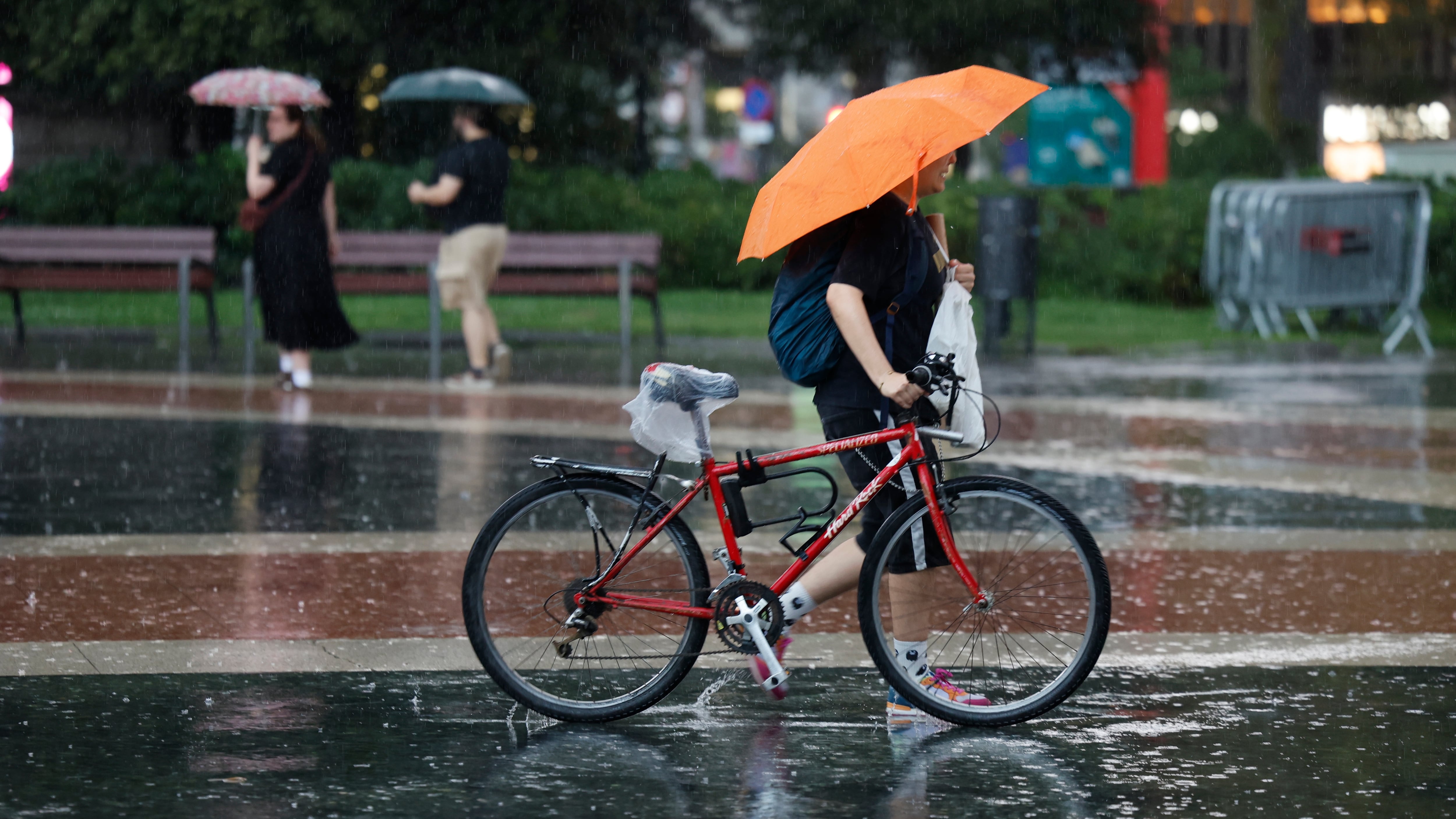 Una persona en bici se protege de la lluvia en Barcelona. (Toni Albir/EFE)