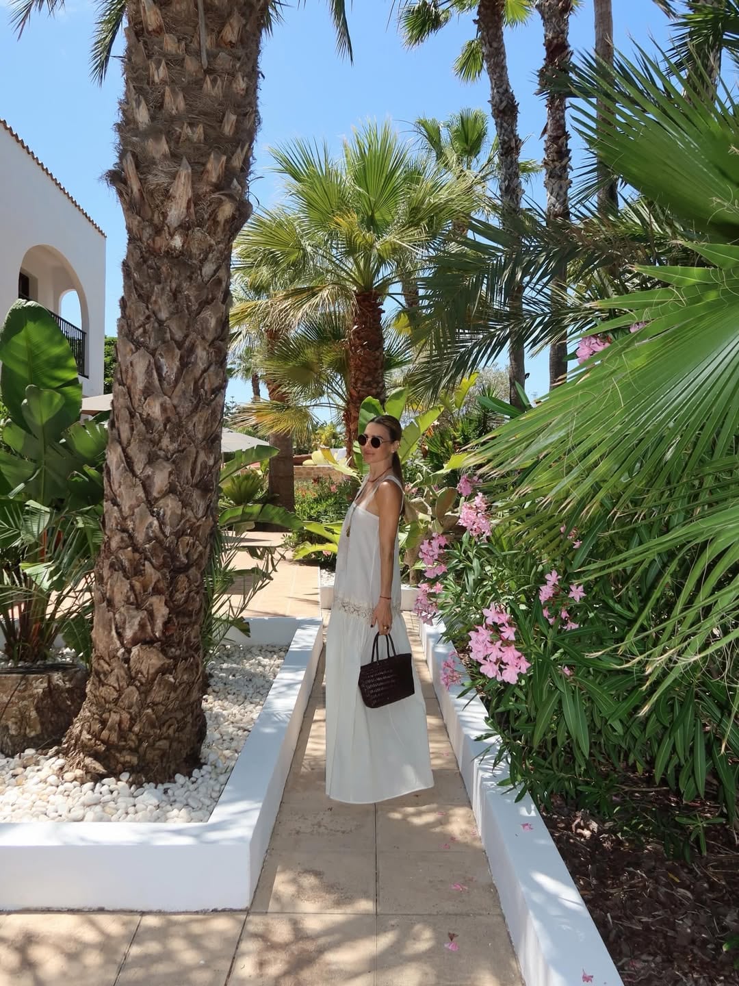 Entre palmeras y adelfas rosas, María Vázquez con vestido largo blanco en los jardines del hotel