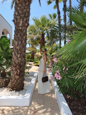 Entre palmeras y adelfas rosas, María Vázquez con vestido largo blanco en los jardines del hotel