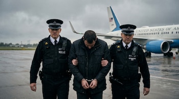 Hombre esposado con la cabeza baja, flanqueado por dos policías uniformados, camina en una pista de aeropuerto. Avión "UNITED STATES OF AMERICA" de fondo.