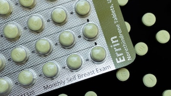 Primer plano de píldoras anticonceptivas de color verde claro en un blíster plateado y algunas sueltas sobre una superficie oscura