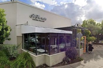 Exterior de un restaurante con el cartel Il Fornaio Cucina Italiana, una terraza de vidrio, arbustos y dos personas paradas en la acera