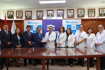 Nueve personas en trajes formales y batas médicas posan detrás de una mesa de madera sosteniendo un recipiente cilíndrico transparente