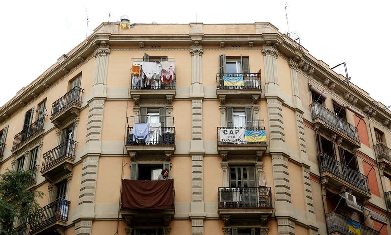 Una pancarta contra los apartamentos turísticos en un balcón mientras una mujer tiende la ropa. La pancarta dice