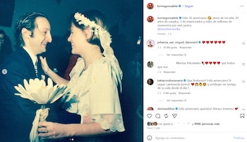 Hombre de traje y mujer con vestido blanco y tocado floral en una boda de época, ambos sonríen mirándose, la mujer sostiene un ramo de flores blancas