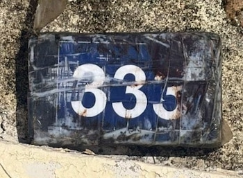 Paquete rectangular envuelto en cinta plástica con el número 335 en blanco sobre fondo azul, apoyado sobre una superficie rugosa