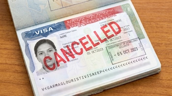 Primer plano de un pasaporte abierto mostrando una visa de Estados Unidos con el sello rojo "CANCELLED" sobre la foto y los datos personales.