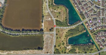 Vista aérea de un área de Miami-Dade con carreteras, terrenos sin desarrollar, cuerpos de agua y un barrio residencial. Un pin rojo marca una intersección