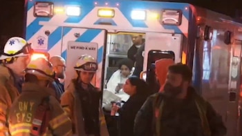 Escena nocturna con una ambulancia de emergencia, sus puertas abiertas y luces intermitentes. Socorristas rodean el vehículo, y una persona está dentro