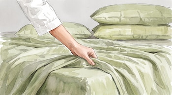 Una mano sostiene una sábana de color verde sobre una cama con tres almohadas al fondo.