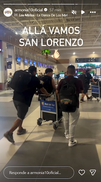 Tres hombres empujan carritos de equipaje en un aeropuerto con mostradores de facturación. Se lee el texto "ALLÁ VAMOS SAN LORENZO" y el logo "Mall del Sur"