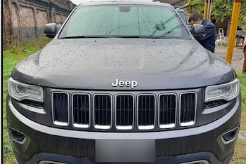 Parte frontal de un vehículo Jeep Grand Cherokee gris con gotas de agua en el capó y una persona parada detrás