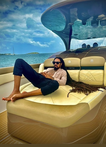 Un hombre con rastas largas y gafas de sol reclinado en un sillón a bordo de un yate frente al mar