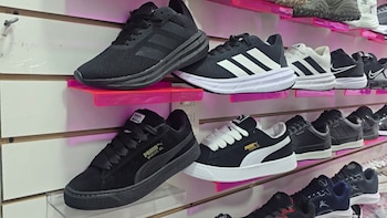 Zapatillas deportivas de colores negro y blanco con diseños similares a marcas conocidas, exhibidas en filas de estantes iluminados con luces rosadas