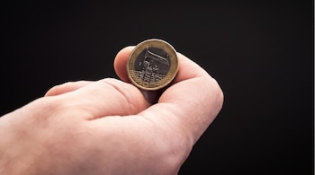 Una mano sostiene una moneda de un euro antes de lanzarla al aire.