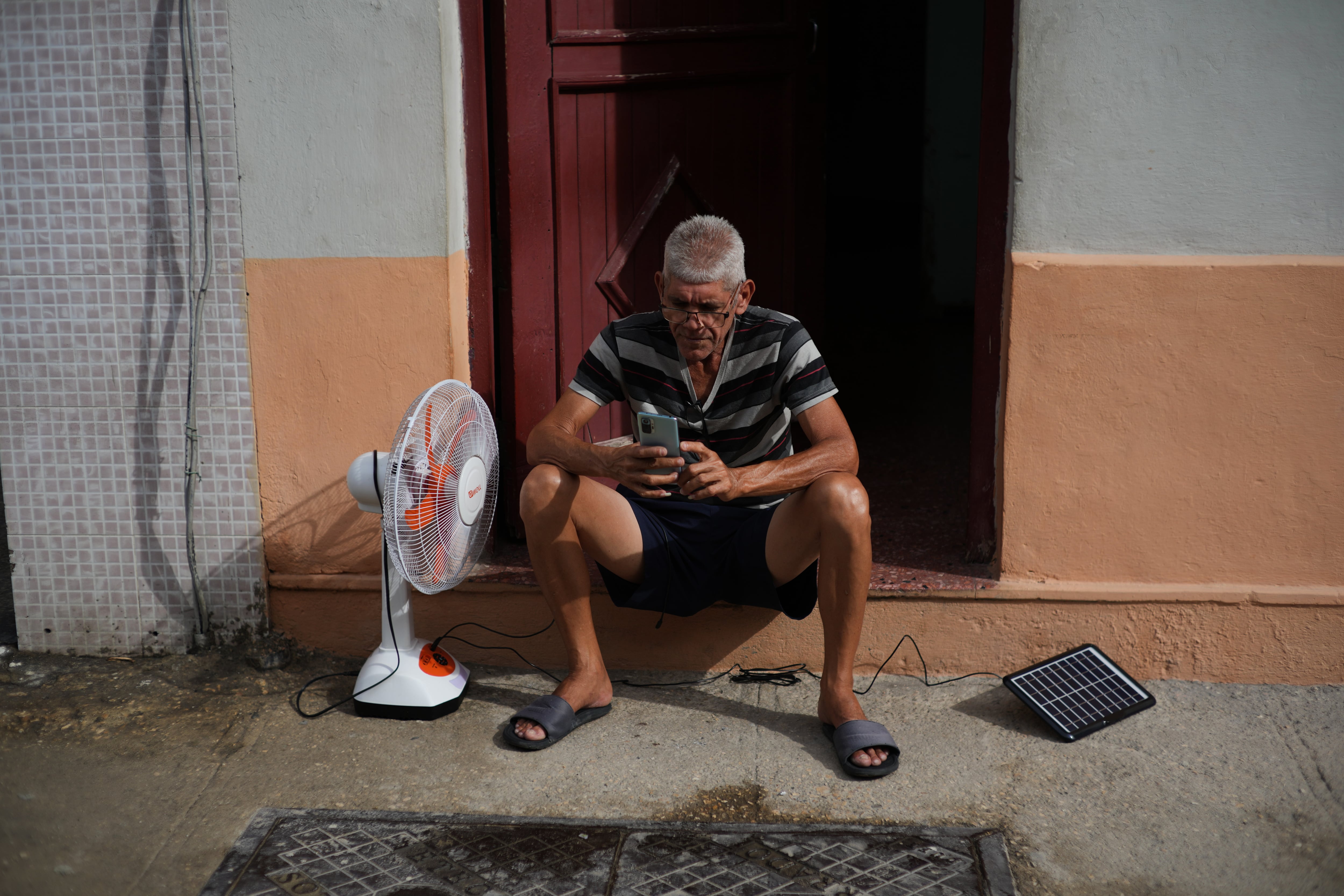 Un hombre carga su ventilador y su teléfono celular con un panel solar durante un apagón en La Habana, el 17 de marzo del 2026 (AP foto/Ramón Espinosa)