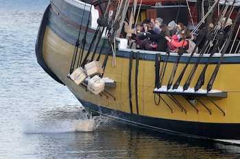 ARCHIVO-En esta foto del lunes 11 de diciembre de 2017, visitantes del Museo del Motín del Té de Boston lanzan réplicas de históricos contenedores de té desde una réplica del buque Beaver, en Boston (AP Foto/Steven Senne)