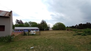 Vista exterior de un edificio con techo de chapa y murales coloridos, junto a un campo de césped con dos arcos de fútbol y árboles bajo un cielo nublado