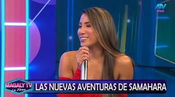 Mujer con cabello largo castaño y vestido rojo sostiene un micrófono en un plató de televisión con luces azules y rosas, y texto en pantalla