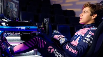 Franco Colapinto, un joven con uniforme de carreras rosa y azul, está sentado en un simulador de carreras con un volante y pedales, concentrado en la pantalla
