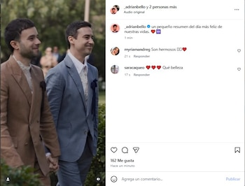 Dos hombres, Bruno Ascenzo y Adrián Bello, vestidos con trajes de colores tierra y azul claro, respectivamente, se toman de la mano y sonríen al aire libre