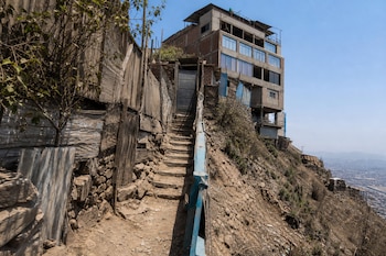 Un camino estrecho de tierra con escalones de cemento sube por una ladera inclinada hacia una puerta metálica cerca de un edificio.