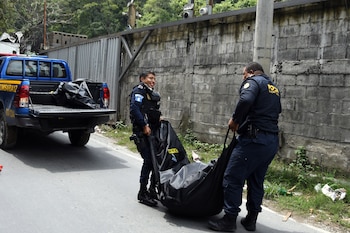 Piernas de un bombero con uniforme negro junto a dos formas cubiertas con plásticos azules y negros sobre el asfalto