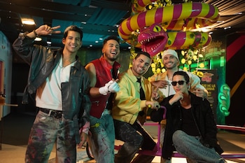 Cinco jóvenes con chaquetas y ropa casual posan sonrientes delante de una gran figura decorativa en forma de serpiente