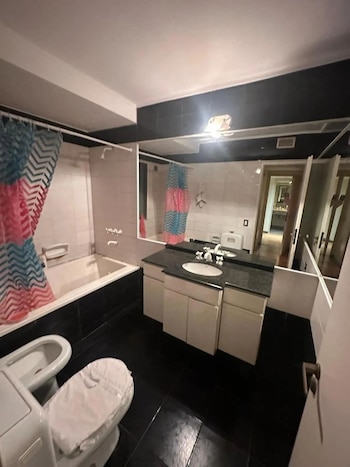 Vista de un baño con piso y paredes superiores negras, paredes intermedias blancas, bañera con cortina multicolor, doble tocador y sanitarios blancos