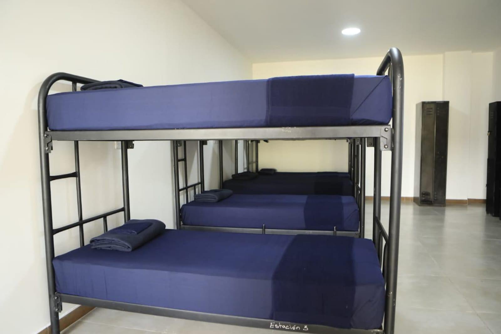 Un dormitorio con varias literas de marcos metálicos y sábanas azules, con taquillas oscuras al fondo, muestra un área de descanso comunal. Guatemala (Ministerio de Gobernación de Guatemala)