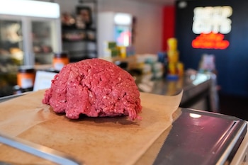Primer plano de un montículo de carne molida roja cruda sobre papel de estraza en una bandeja metálica; fondo borroso de una carnicería o tienda de comestibles