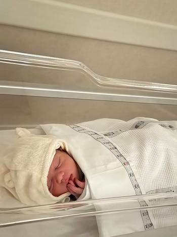 Primer plano de un bebé recién nacido durmiendo plácidamente en una cuna de hospital, envuelto en una manta blanca con un gorro con orejas
