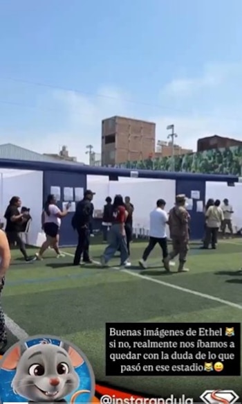 Vista de un campo deportivo con césped artificial donde varias personas caminan junto a estructuras temporales blanco-azuladas, bajo un cielo claro