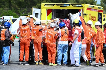 Personal de emergencia con uniformes naranjas y blancos rodea una camilla con una persona cubierta con una manta térmica, cerca de una ambulancia amarilla