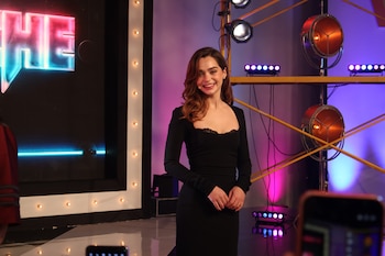 Una mujer con un vestido negro sonríe en un escenario decorado con luces y letreros de neón