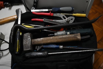 Varias herramientas manuales se ven de cerca en una bolsa, incluyendo un martillo de mango de madera, destornilladores, alicates y una palanca de metal