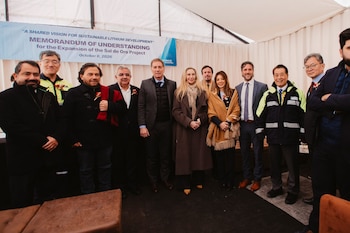 Un grupo de personas formadas en fila posan sonrientes frente a un cartel azul que anuncia el proyecto Sal de Oro