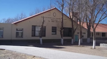 Edificio de hospital beige con techo de tejas rojas, árboles desnudos y un sendero de pavimento. En la fachada, el nombre Hospital Dr. Jorge Uro y la afiliación