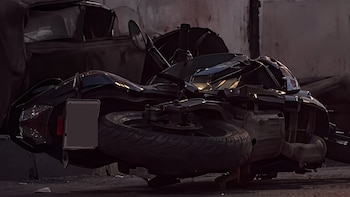Motocicleta de color oscuro volcada sobre el suelo, con neumáticos y una matrícula rectangular visible en la parte trasera